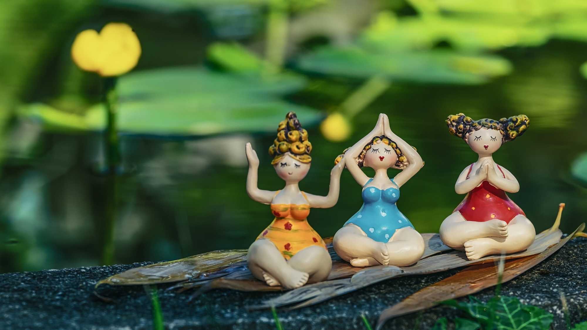 3 colourful ceramic figures doing yoga poses by a pond
