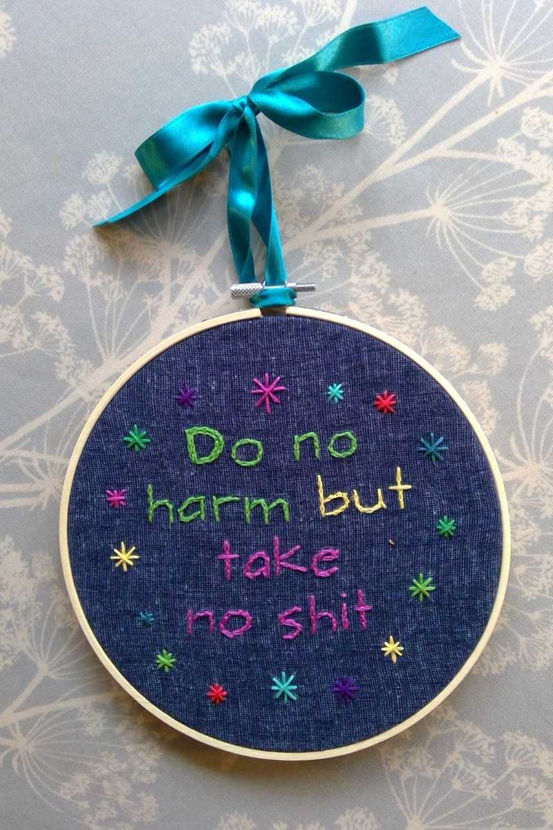 Embroidery hoop with the words "Do no harm but take no shit" in green, yellow and pink letters on a dark blue fabric
